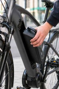 Main retirant la batterie amovible d'un vélo électrique de ville, en milieu urbain. Critère essentiel pour choisir son VAE : capacité et amovibilité de la batterie.