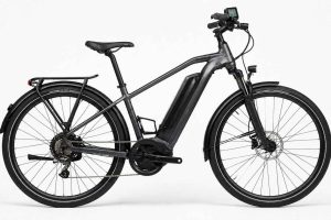 Vélo électrique de ville photographié de profil sur fond blanc en studio. Batterie intégrée au cadre, affichage LCD au guidon et freins hydrauliques bien visibles. Guide comparatif des meilleurs VAE Decathlon 2026