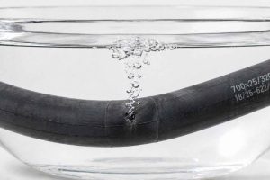 Gros plan d'une chambre à air de vélo plongée dans un bol d'eau claire. Des bulles remontent à la surface à l'emplacement de la perforation. Technique simple et efficace pour localiser une crevaison de vélo.