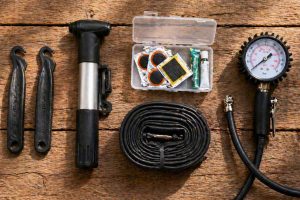 Vue de dessus d'un kit de réparation de crevaison vélo posé sur une surface en bois : démonte-pneus, pompe portable, rustines, chambre à air neuve et manomètre. L'essentiel à emporter en sortie vélo pour faire face à un pneu à plat.